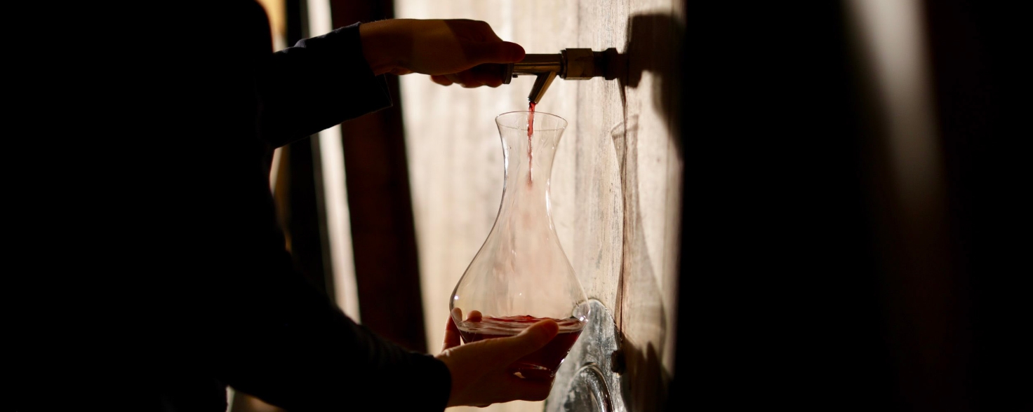 hand collecting red wine in a carafe from a barrel
