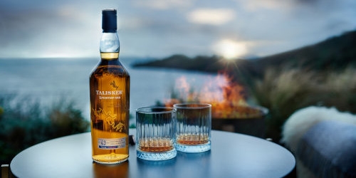 Bottle with two glasses on a table with sunset and sea behind