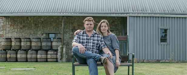 couple sitting on a bench outside building with barrels