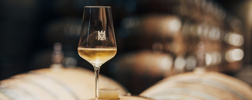 A white wine glass in a room full of wine barrel