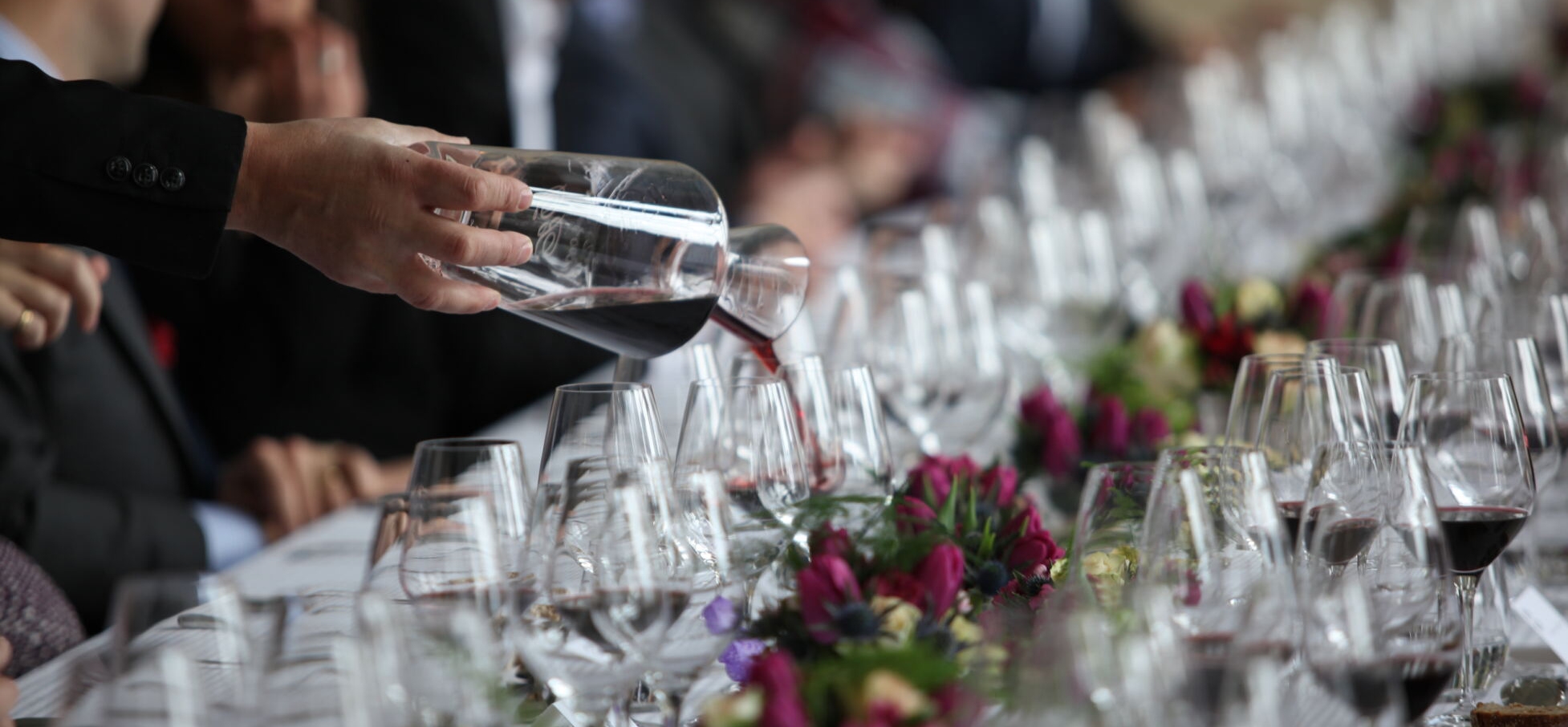 man pouring red wine into a wine glass on a formal table setting