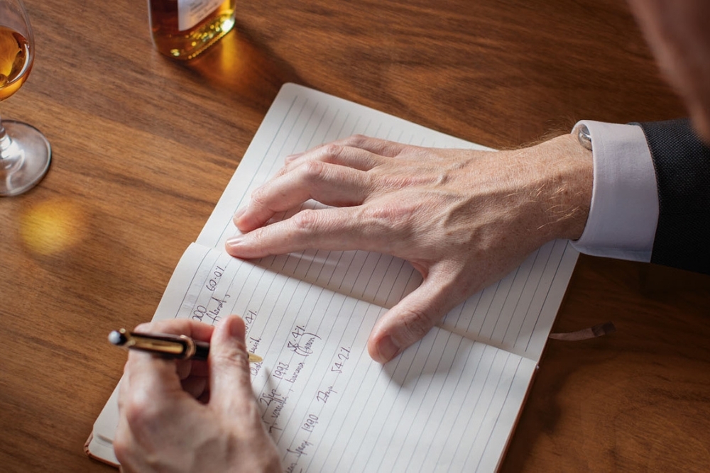 Person Writing in Book with Whisky
