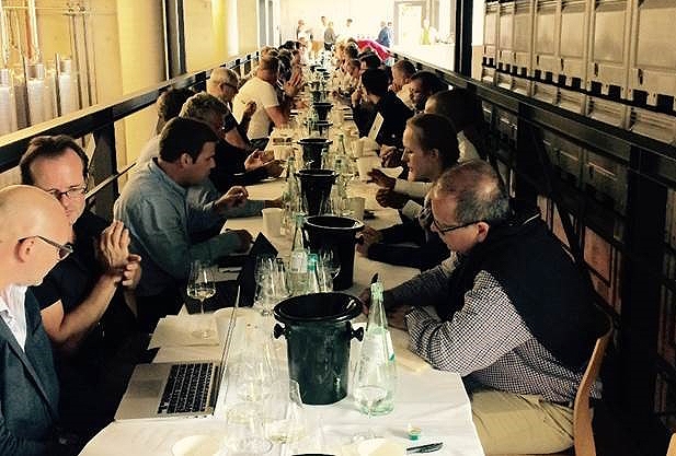 People sitting at a long table with glasses of wine and laptops