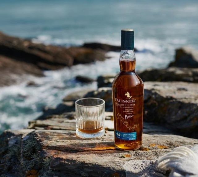 bottle and glass of whisky on rocks beside sea