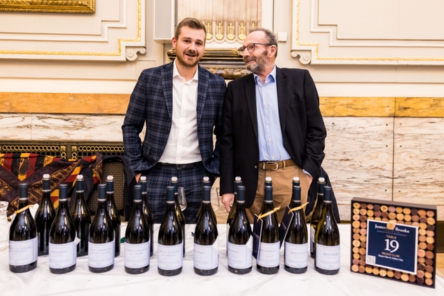 two men with their arms around eachother in front of a selection of wine bottles