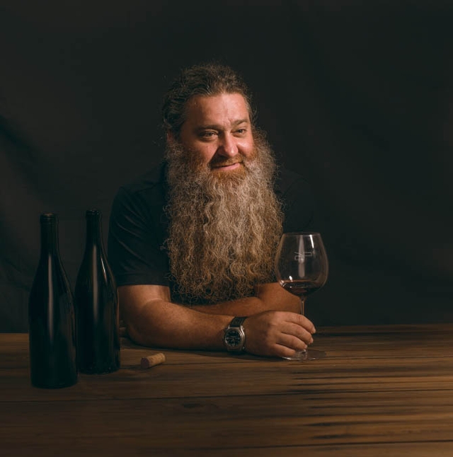 Man with beard sitting at table with glass of wine