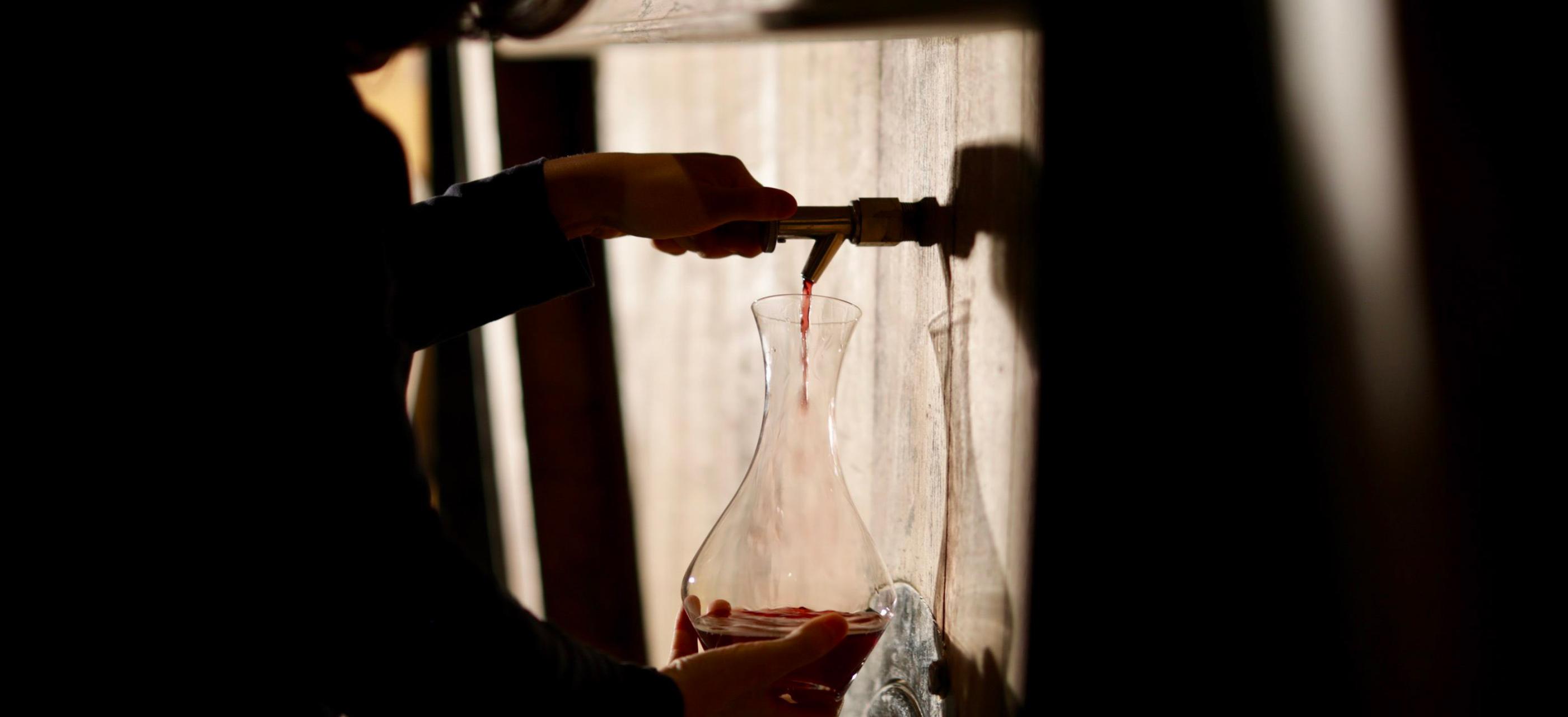 close up of hands filling a jug with red wine from a wine barrel