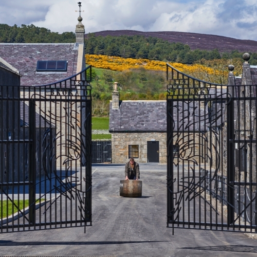 gates leading into a stone distillery with hills in the background