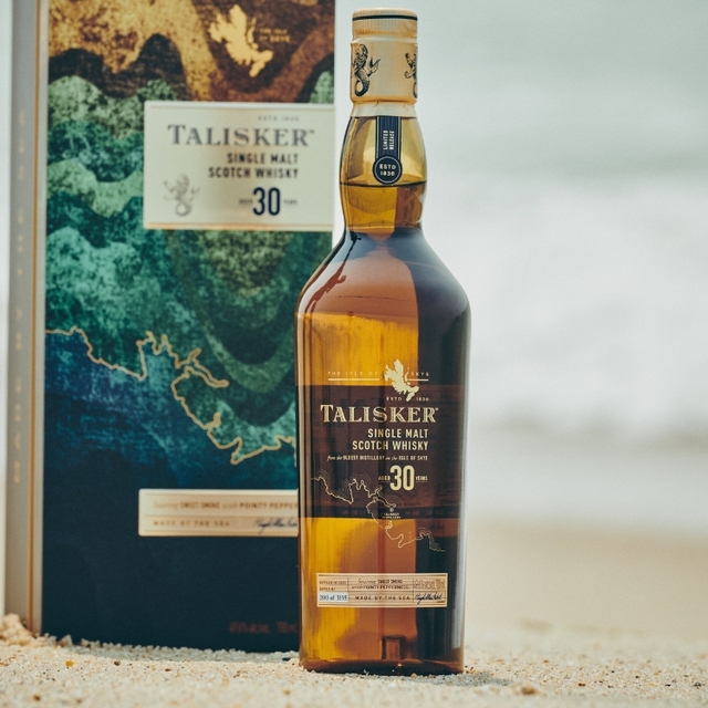 talisker whisky bottle on the beach next to a branded box with wave design