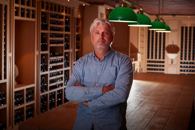 man standing with arms crossed in front of a wine cellar